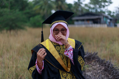 Portrait of woman in graduation gown sitting on log