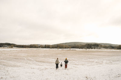 Lesbian mothers and daughter running on snow covered land