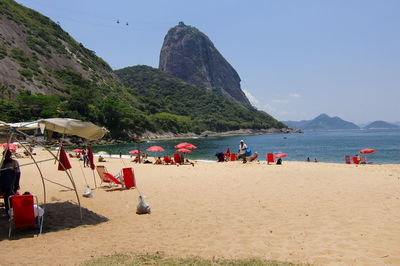 Umbrellas and deck chairs at beach against rocky mountains on sunny day