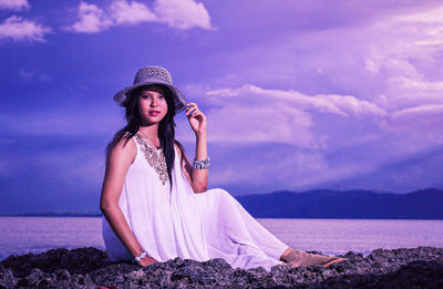 Portrait of young woman sitting against sea against sky against sunlight