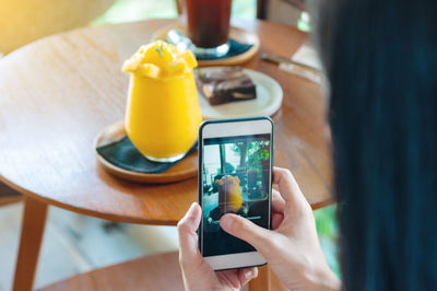 Midsection of person photographing with mobile phone on table