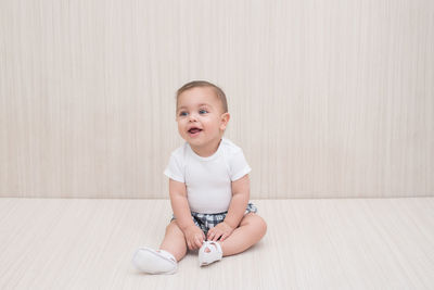 Cute boy looking away while sitting on floor against wall