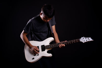 Man playing guitar against black background