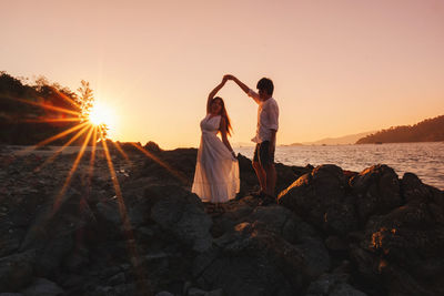 Friends standing on rock against sky during sunset