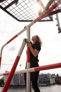 Low angle view of woman climbing on built structure against sky