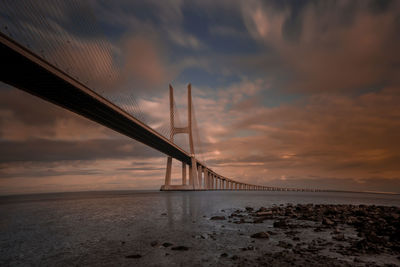 Suspension bridge over sea against cloudy sky