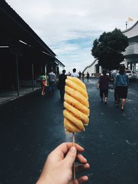 Cropped hand of man holding ice cream on road against sky