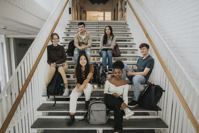 Portrait of happy multiracial male and female students sitting on staircase in university