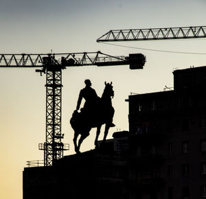 Low angle view of silhouette crane against building