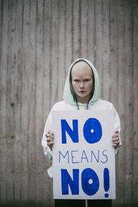 Portrait of female activist holding no means no poster against wall