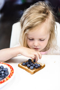 A little cute girl is eating her breakfast toast with blueberries