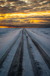 Tire tracks on snowy road during sunset