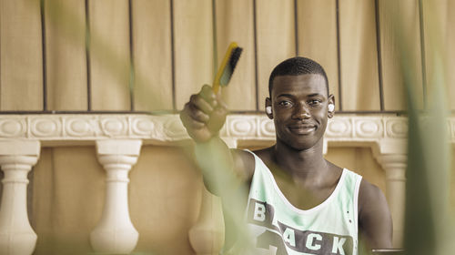 Black man in sporty tank top lifting a hairbrush while sitting on a bench in coffee shop