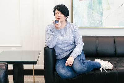 Middle age brunette woman sitting on couch sofa at home and talking on audio chat phone with friends