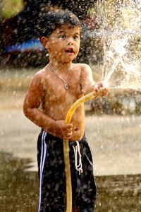 Shirtless boy spraying water from hose in yard