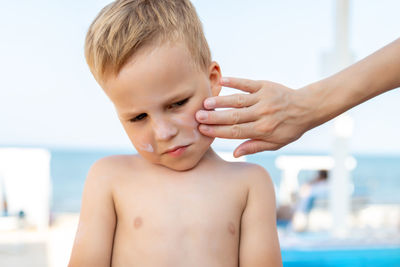 Hands of woman applying suntan lotion on boy's face