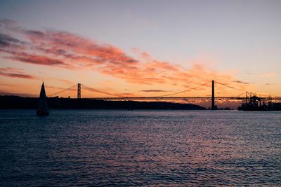 Silhouette 25 de abril bridge over tagus river against sky during sunset