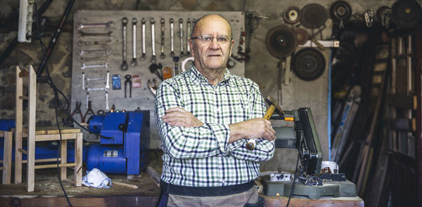 Portrait of smiling senior man with arms crossed standing in workshop