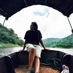 Young man sitting on boat against sky