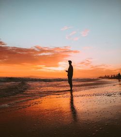 Silhouette man standing on shore at beach against sky during sunset