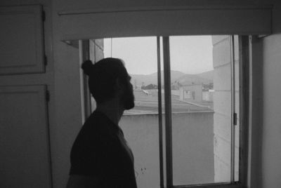 Side view of man looking through window