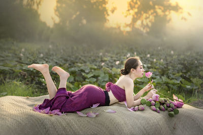 Full length of beautiful woman resting on textile with lotus flowers on land