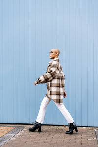 Woman with shaved head walking on footpath by blue wall