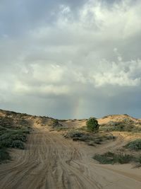 Dirt road amidst desert land against sky