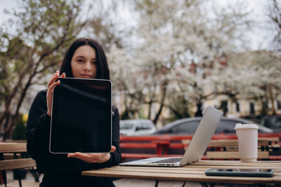 Young woman using digital tablet while sitting on table