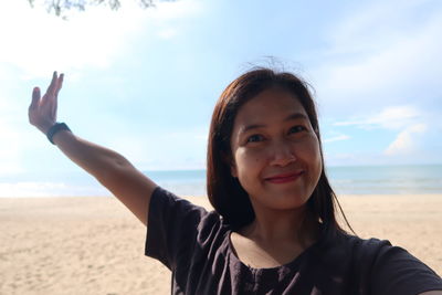 Portrait of smiling young woman on beach against sky