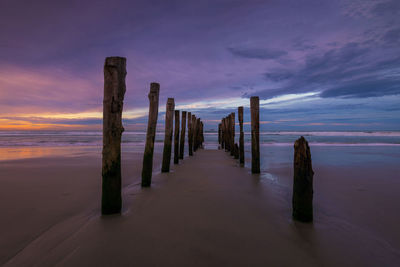 Wooden posts on beach against sky during sunset at st. clair beach, dunedin, new zealand