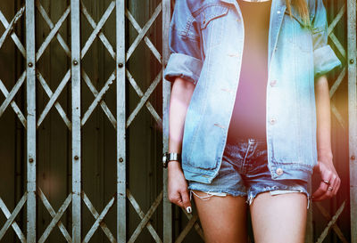 Midsection of woman wearing denim jacket standing against gate
