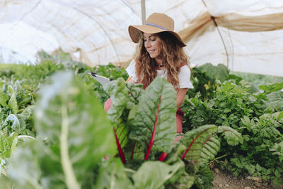 Smiling farmer taking inventory of vegetables at greenhouse