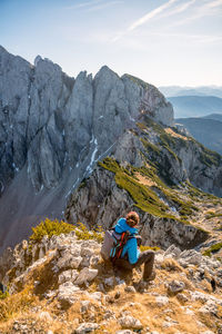 Man sitting on rock by mountains against sky