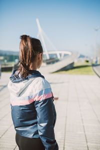 Young woman standing on sidewalk against sky