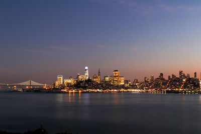 Illuminated city by river against sky at night