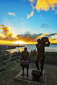 Men standing on sea shore against sky during sunset