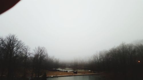 Bare trees on landscape against sky during winter