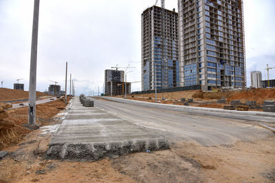 Road by buildings against sky in city