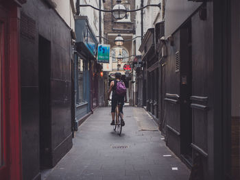 Rear view of woman riding bicycle in alley