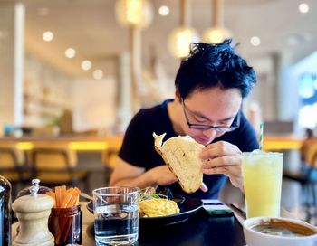 Young man in eyeglasses working on smartphone while eating breakfast in cafe.