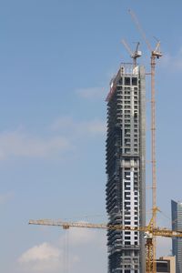 Low angle view of crane by building against sky