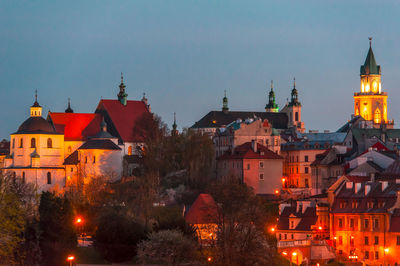 Illuminated buildings in city against clear sky at dusk