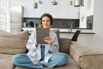 Young woman using digital tablet while sitting on sofa at home