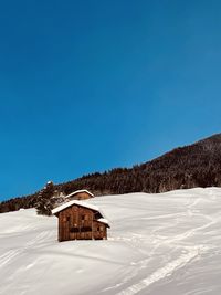 Traditional built structure on snow covered alpine land against clear blue sky