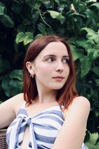 Beautiful young woman looking away while sitting against plant