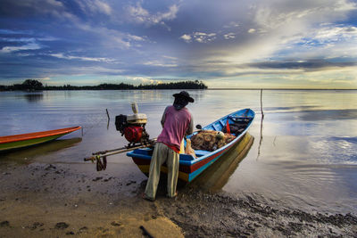 Man sitting on boat moored at sea shore against sky