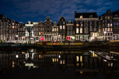 Illuminated residential buildings by canal against sky at dusk