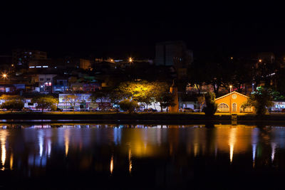 Illuminated buildings by river against sky at night