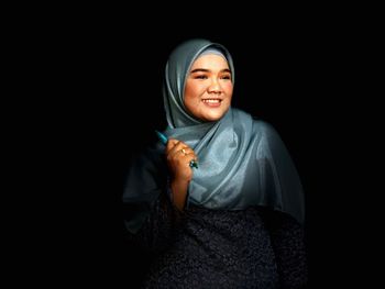 Smiling woman wearing hijab against black background